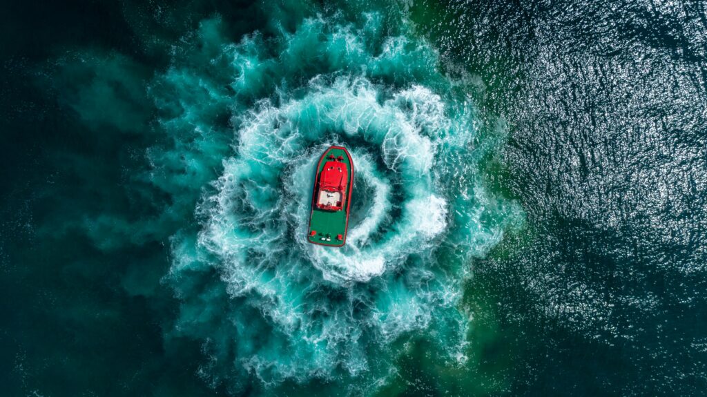 pexels-photo-1555313-1555313 Red motor boat making spiral waves on turquoise ocean in aerial view, shot by drone.